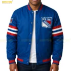 Men’s blue varsity jacket with full-snap front closure, ribbed cuffs and waistband, embroidered chest patch, and red-and-white striped sleeves, styled with denim pants.